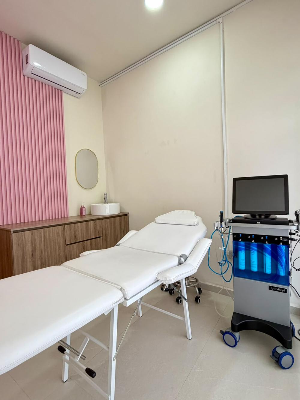 Cabina privada con camilla blanca, muro acanalado rosa y equipo HydraFacial
